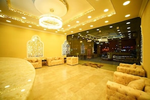 Um hall de entrada com piso de mármore, área de estar com sofás, lustre e parede de vidro com reflexos.