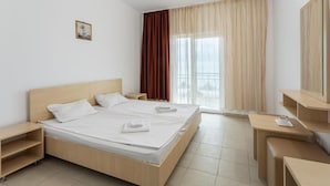 A hotel room with a double bed, a bedside table, a desk with a chair, a large window with curtains, and a small picture on the wall. - Vraja Marii Eforie Nord (Eforie)