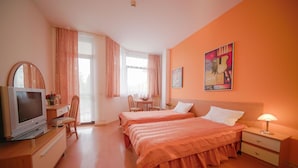 Une chambre d’hôtel avec deux lits, une télévision, un bureau avec une chaise et une table à manger avec des chaises.