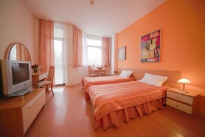 A hotel room with two beds, a TV, a desk with a chair, and a dining table with chairs. - Apartments Flora (Samokov)