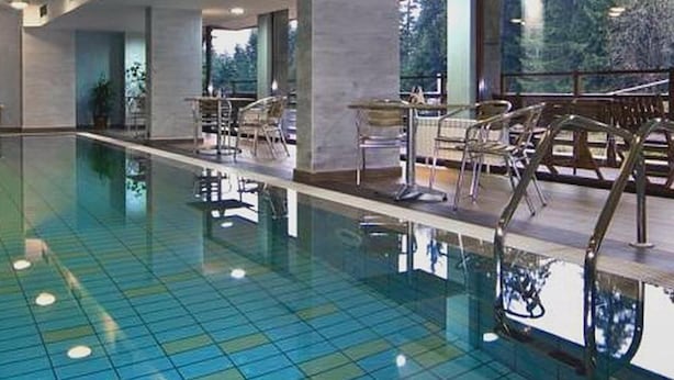Une piscine aux carreaux bleu clair, entourée de chaises longues et d’une terrasse en bois.