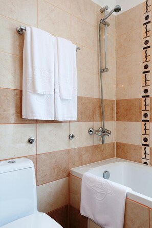 A bathroom with a bathtub, a shower, and a toilet. There are two white towels hanging on the wall. - Apartments Flora (Samokov)