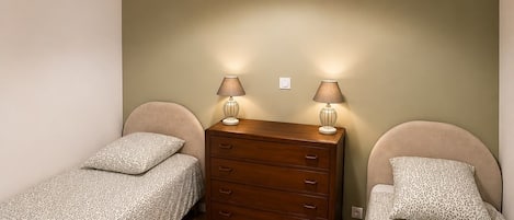 A bedroom with two single beds, a wooden dresser, and a hanging light fixture.
