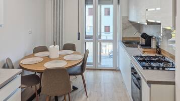 Een moderne keuken met een centraal eiland, een eethoek met een ronde tafel en uitzicht door de glazen deuren.