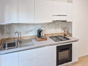 A modern kitchen with a stainless steel sink, a coffee machine, a gas stove, and an oven.