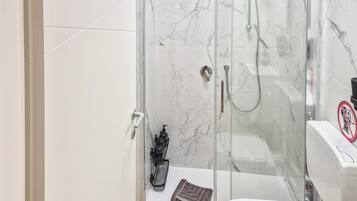 Un baño moderno con ducha separada por mampara de vidrio, inodoro y lavamanos.