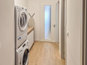 A laundry room with stacked washing machines and dryers, a wooden floor, and a frosted glass door.