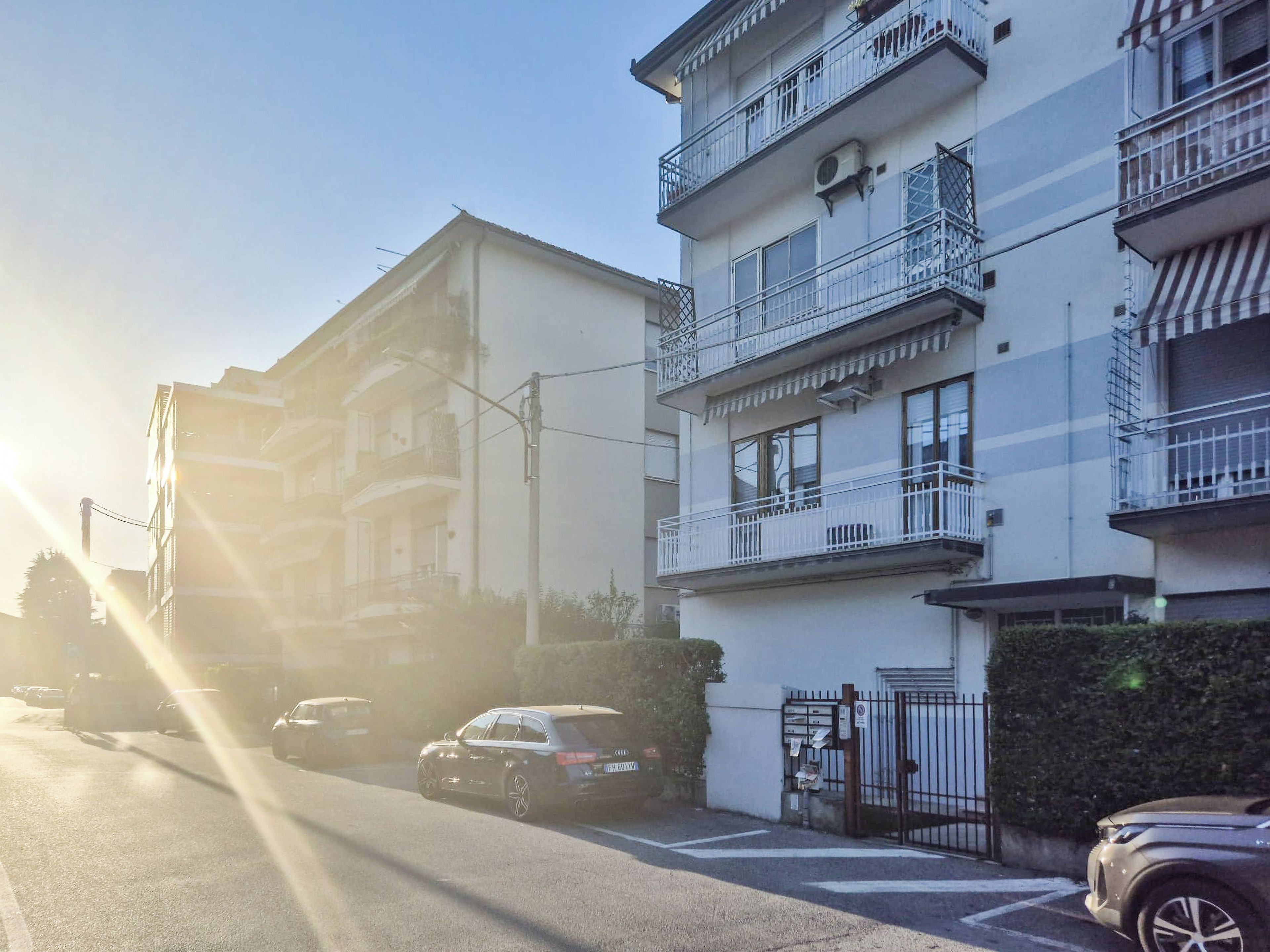 Un immeuble résidentiel à plusieurs étages, doté de balcons, d’une entrée sécurisée et de voitures garées.