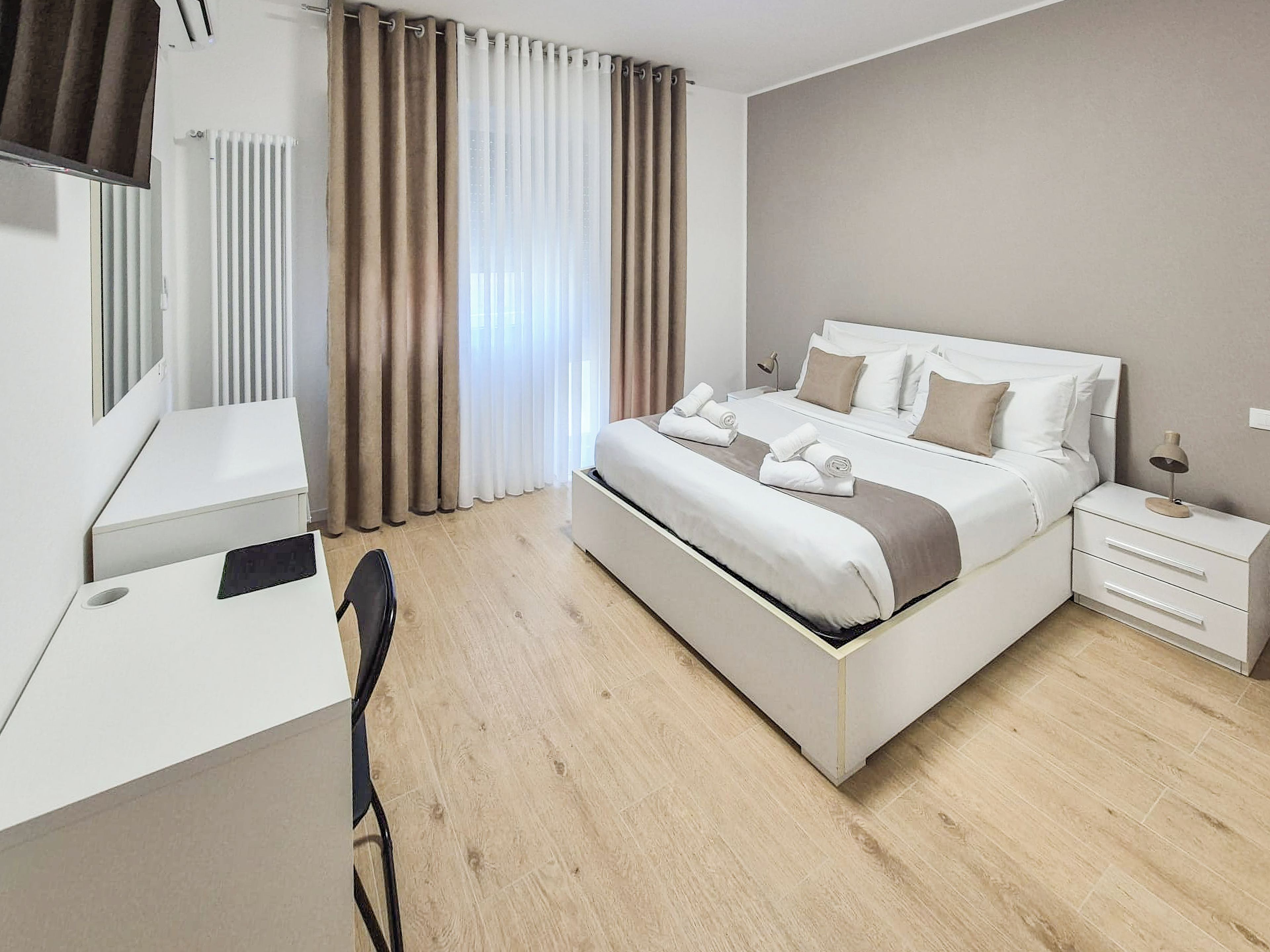 A hotel room with a bed, bedside tables, a desk, and a chair.