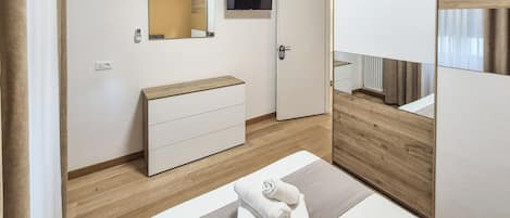 A modern bedroom with a bed, a bedside table, a dresser, a mirror, and a television.