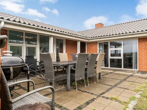 Eine Terrasse im Freien mit Esstisch und Stühlen, einem Grill und einem Ziegelgebäude mit großen Fenstern.