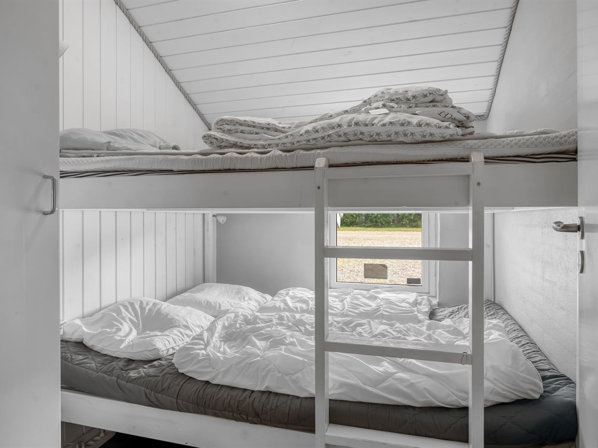 A bunk bed room with a ladder, a window, and a view of the outside.
