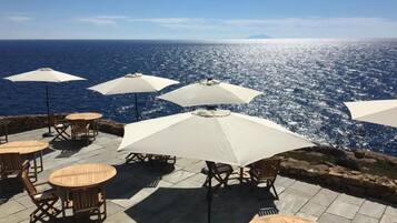 Un espace extérieur aménagé avec des tables, des chaises, des parasols et une vue sur l’océan.