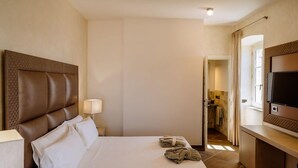 Ein Hotelzimmer mit einem großen Bett, einem Fernseher, einem Schreibtisch und einem durchgegangenen Badezimmer.