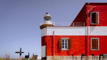 Un bâtiment rouge et blanc avec un phare, des tables à l’extérieur et un ciel dégagé.