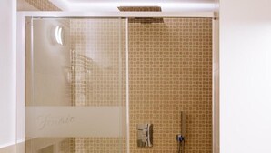 Eine gläserne Duschkabine mit einer Fliesenwand, einer Handbrause und einem Handtuch auf dem Boden.