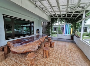 An outdoor seating area with a long wooden table and stools, surrounded by a tiled floor and a covered pergola. - Li Wu Zuo Can B&B (Xiulin)