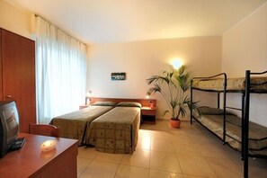 Una camera d'albergo con due letti, una scrivania, una sedia, un televisore, una pianta in vaso e un letto a castello.