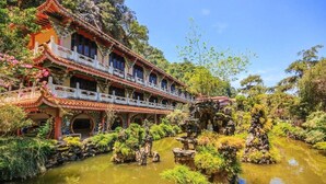 A traditional building with multiple balconies, a pond with rocks and plants, and a clear sky. - Silver Star Hotel (Brinchang)