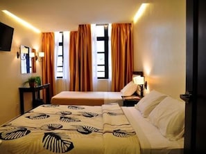 Quarto de hotel com duas camas, televisão, mesa de cabeceira e janela com cortinas.