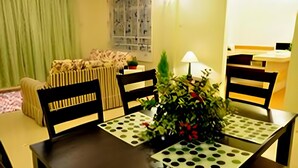 A dining area with a table set for four, chairs, a vase with greenery, and a window with a view of buildings. - Silver Star Hotel (Brinchang)