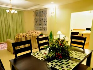 Uma área de refeições com mesa posta para quatro pessoas, cadeiras, um vaso com folhagem e uma janela com vista para edifícios.