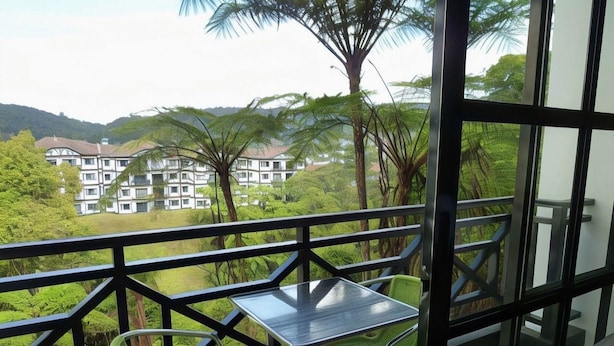 A balcony with a table and chairs, overlooking a lush green landscape and a building in the distance. - Silver Star Hotel (Brinchang)