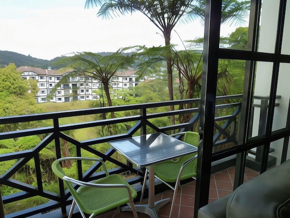 Varanda com mesa e cadeiras, com vista para uma paisagem verdejante e um edifício ao longe.