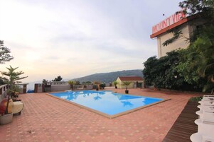Una piscina con vistas a las montañas, rodeada por una zona pavimentada con sillas de descanso y un edificio con el letrero 'MOUNT VIEW'.
