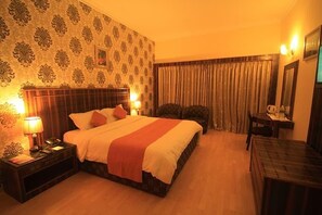 A hotel room with a bed, bedside table, lamp, chair, and a desk. - Howard Johnson Ooty India (Ootacamund)