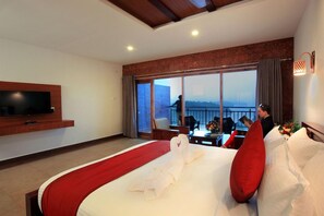 A hotel room with a large bed, a flat-screen TV mounted on the wall, and a balcony with a view. - Arayal Resorts: A Unit of Sharoy Resort (Vythiri)