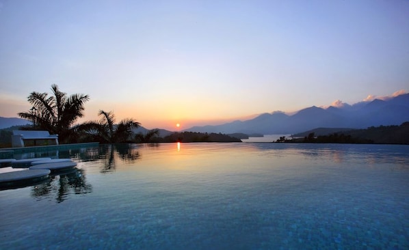 A serene pool area with a sunset view, palm trees, and a mountain backdrop. - Arayal Resorts: A Unit of Sharoy Resort (Vythiri)