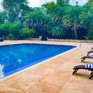 A swimming pool with a tiled deck, lounge chairs, and lush greenery in the background. - Club Mahindra Bharatpur (Bharatpur)