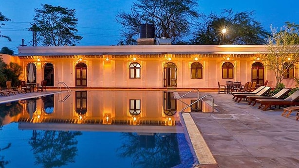 A hotel with a swimming pool, outdoor seating, and a reflection of the building. - Club Mahindra Bharatpur (Bharatpur)