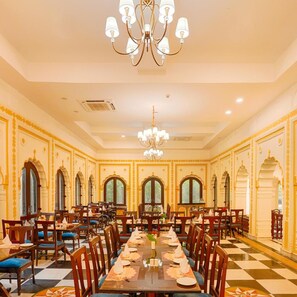 A spacious dining hall with a long table set for a meal, surrounded by chairs, and a chandelier above. - Club Mahindra Bharatpur (Bharatpur)