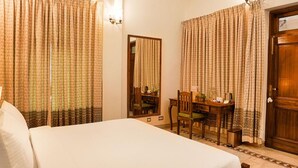 A hotel room with a bed, a desk, and a chair. There is a mirror on the wall and a door with a handle. - Club Mahindra Bharatpur (Bharatpur)