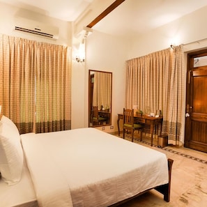 Une chambre d’hôtel avec un lit, un bureau et une chaise. Il y a un miroir au mur et une porte avec une poignée.