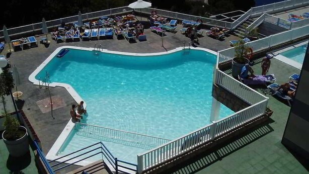 Ein Poolbereich mit klarem, blauem Pool, Liegestühlen und einer Treppe, die hinunterführt.