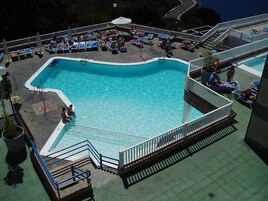 Uma piscina com deck ao redor, cadeiras de descanso e escadaria para um nível superior.