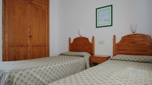 Ein Schlafzimmer mit zwei Holzbetten, einem Kleiderschrank, einem Nachttisch und einem gerahmten Bild an der Wand.