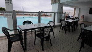 Ein Poolbereich mit Tischen und Stühlen und Blick auf den Pool, sowie ein Schild mit Kontaktdaten.