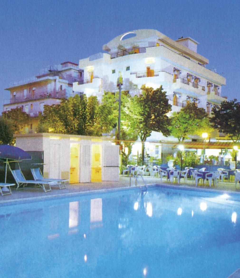 A swimming pool with lounge chairs, a building with multiple balconies, and outdoor seating.