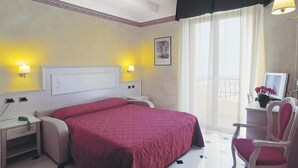 Hotellihuone, jossa on sänky, yöpöydät, työpöytä tuolilla, ikkuna verhoilla ja seinään kiinnitetyt lamput.