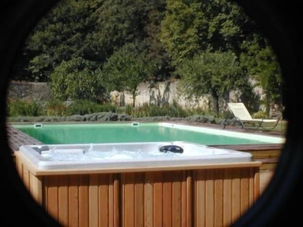 Un bain à remous avec vue sur une piscine et des arbres.