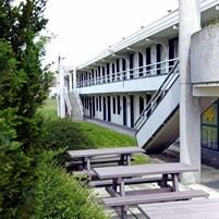 Un edificio con una galería techada, asientos al aire libre y una escalera que conduce a un nivel superior.