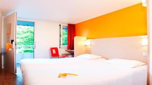 Habitación de hotel con dos camas, una silla roja, una ventana con cortinas y una puerta que da al exterior.