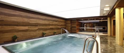 An indoor swimming pool with a wooden wall, a clear ceiling, and a modern design.