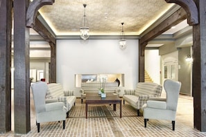 A spacious living room with a brick-patterned floor, two armchairs, a coffee table, and a fireplace. - Aubrecht Country Resort And Spa (Przechlewo)