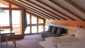 Een kamer met een schuine plafond, een bed met kussens, een bank, een bureau en een stoel.