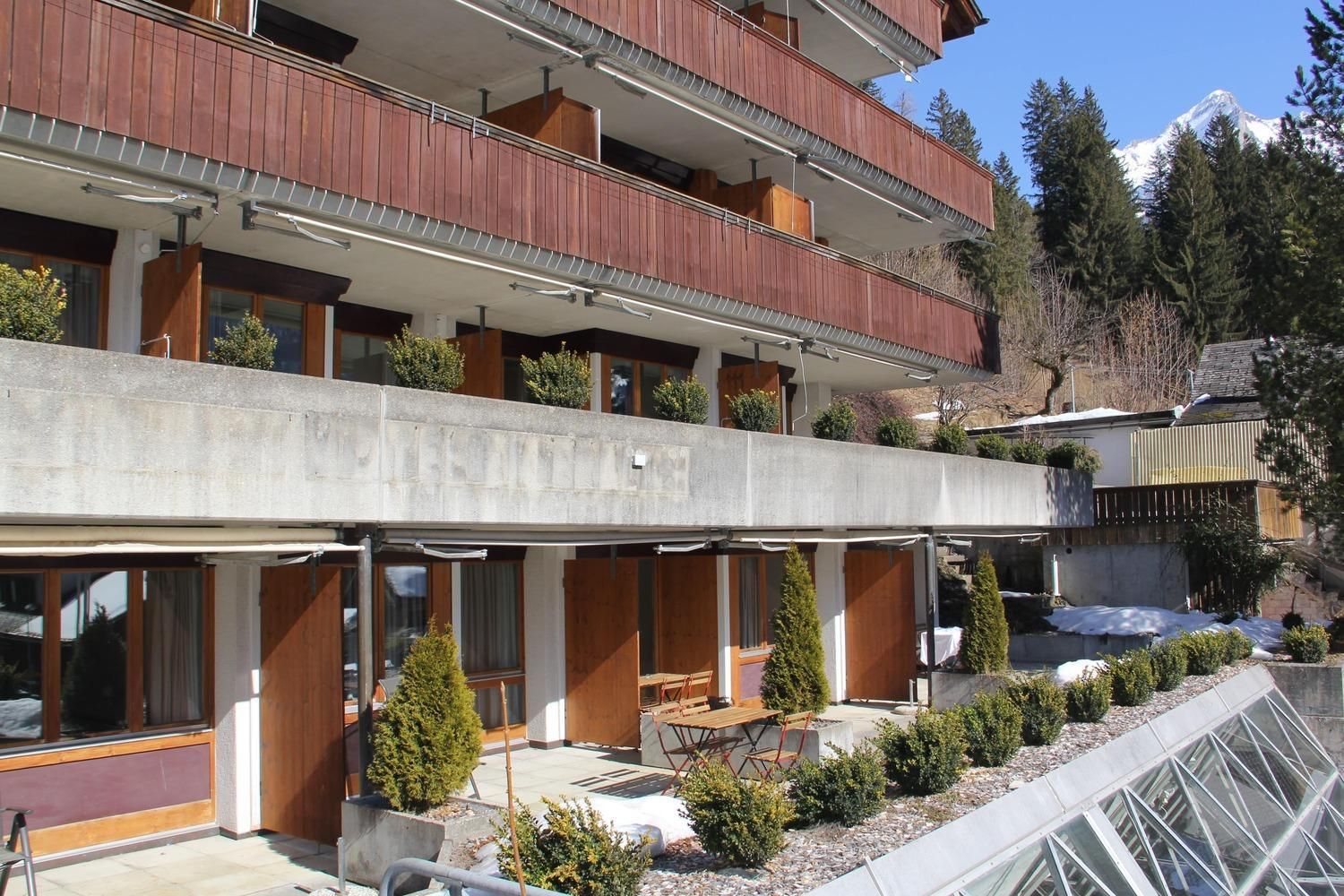 A multi-story hotel with balconies, outdoor seating, and a view of a mountain.